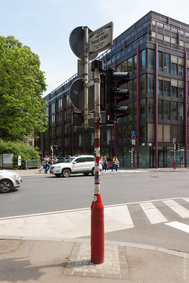 A whole column with traffic signs and a street name plate is mounted to a traffic light