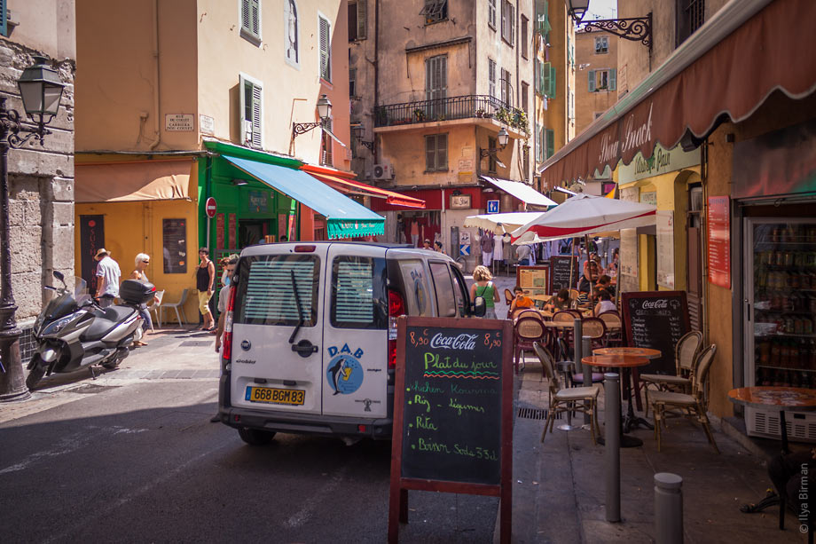 People, motorollers, tables and cars share the streets of Nice